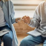Two people holding hands in a therapy session, symbolizing support and recovery at Acadia Healthcare.