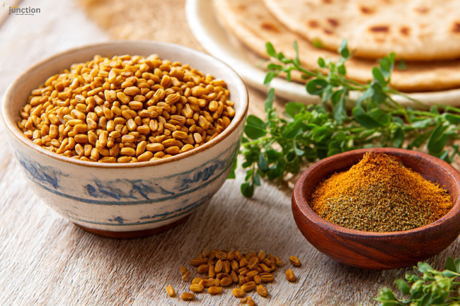 Foenegriek seeds in a bowl next to curry powder, with flatbreads and fresh herbs in the background, showcasing its culinary use.